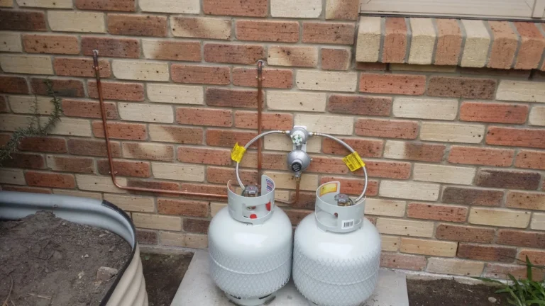 Two LPG cylinders with a changeover regulator against a brick wall